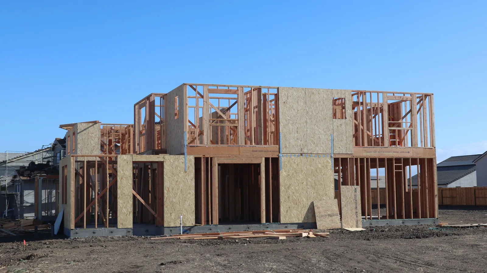 A two-story house in wood framing and sheathing under a clear blue sky